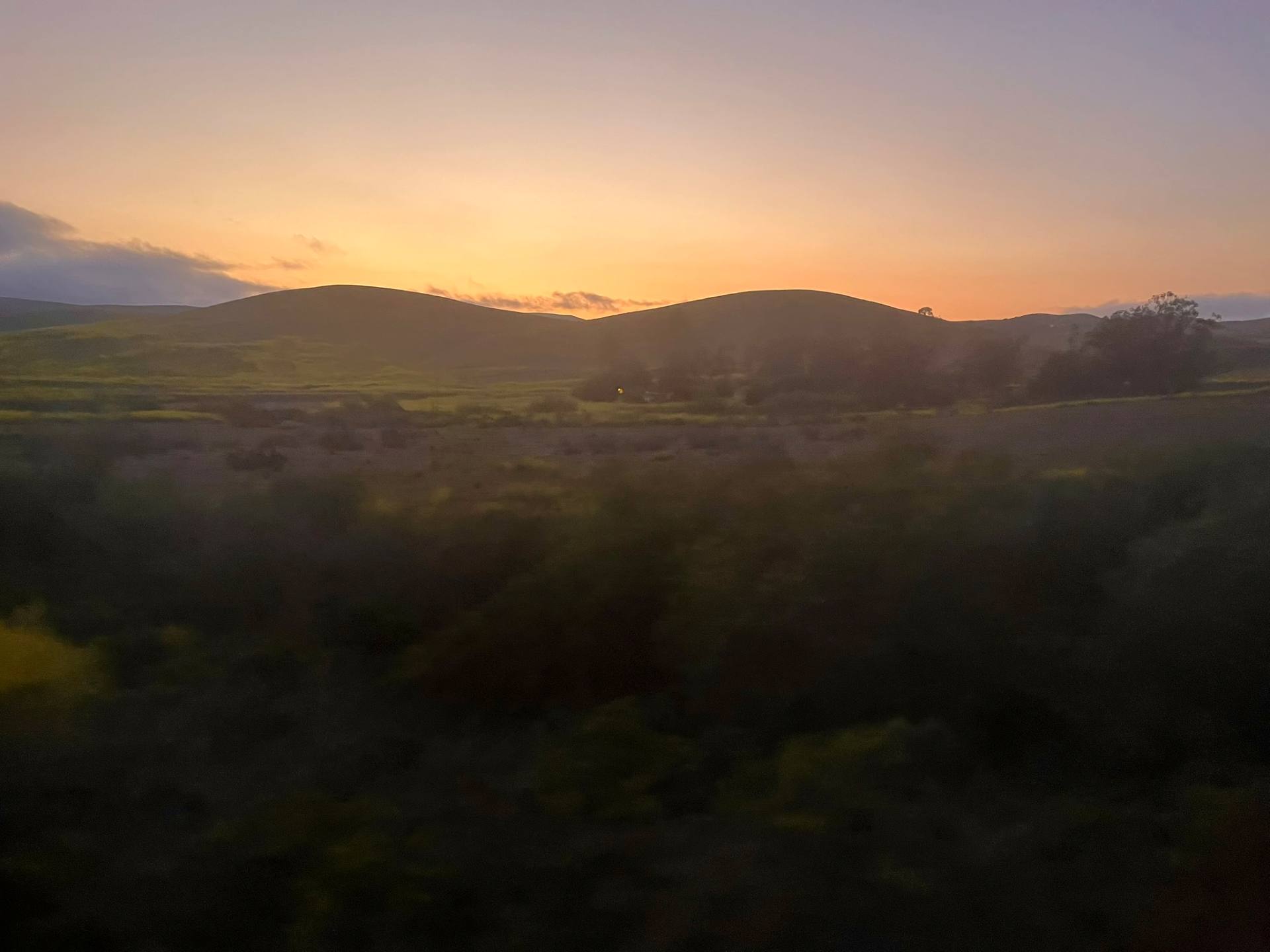 Familiar landscape of SLO with the setting sun's warm glow behind the mountain range. View from Pacific Surfliner.